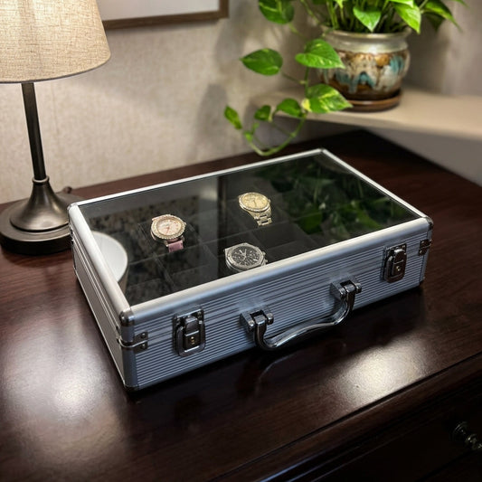 12-slot aluminum watch briefcase closed front view on wooden counter showing watches through glass lid — Grihosojja Bangladesh