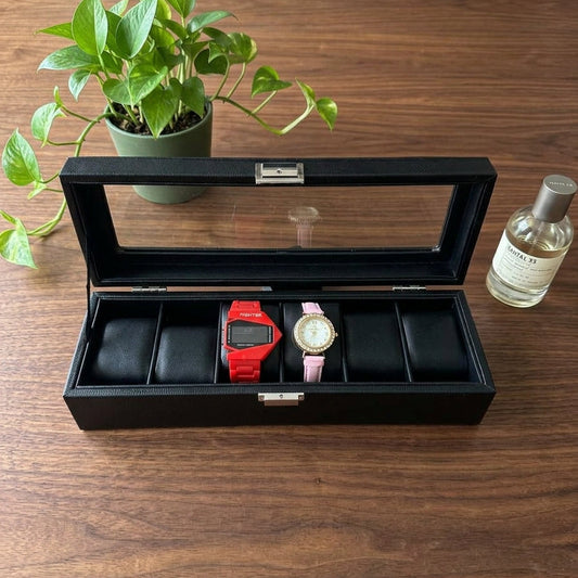"Black 6-slot PU leather watch box with clear glass lid and gold clasp, open to display two watches on a marble surface"